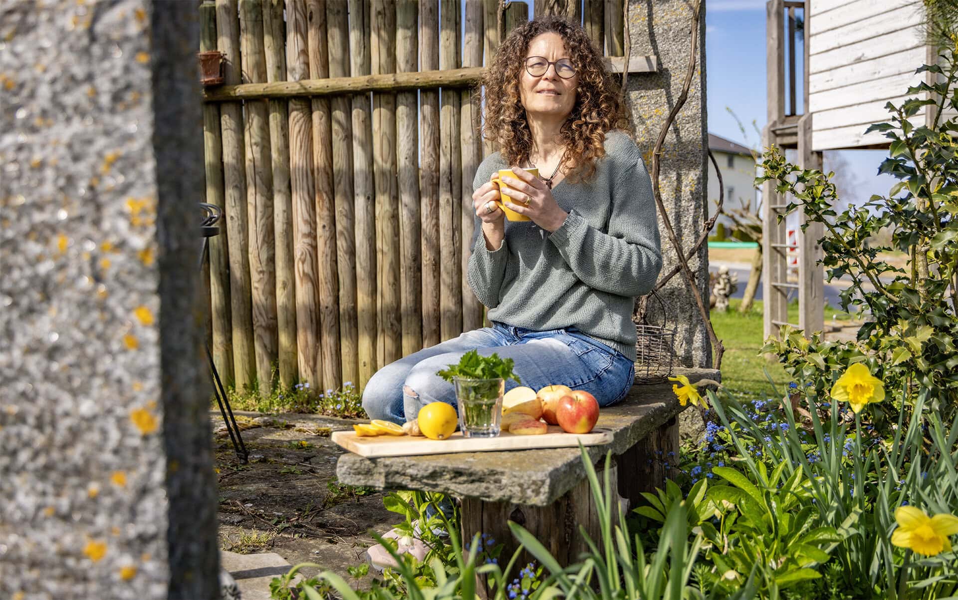 Frau im Garten mit Kaffeetasse und Obst.