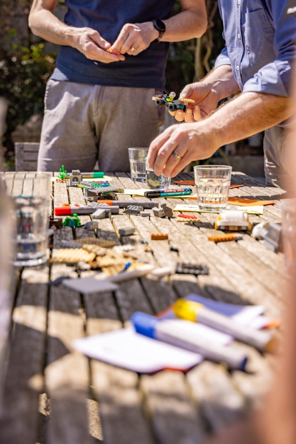 Menschen basteln mit Legosteinen auf Holztisch im Freien