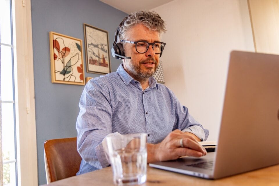 Person mit Headset arbeitet am Laptop zu Hause.