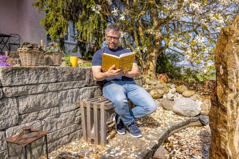 Mann liest Buch im sonnigen Garten.