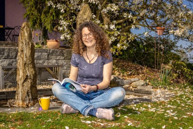 Lächelnde Frau liest im Garten.