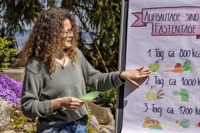 Frau erklärt Fastentage auf Plakat im Freien.